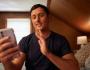 Image of man sitting on a bed using his cell phone.